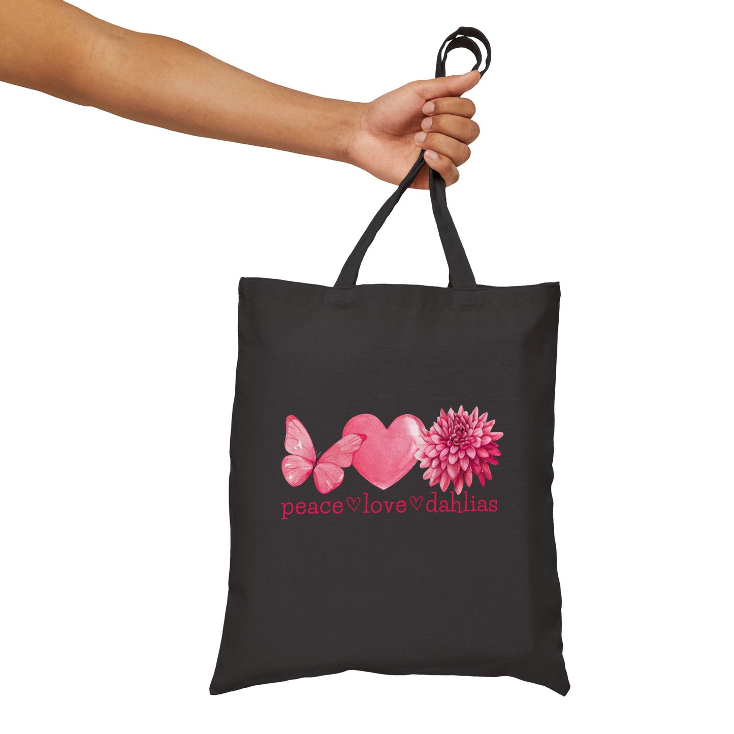 Black tote bag with pink heart, butterfly, and flower design held by a hand on a white background