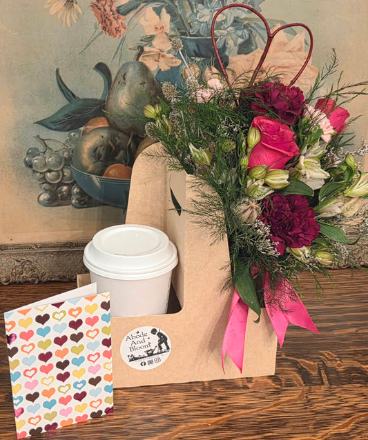 Floral arrangement with a coffee cup, heart-patterned card, and decorative carrier