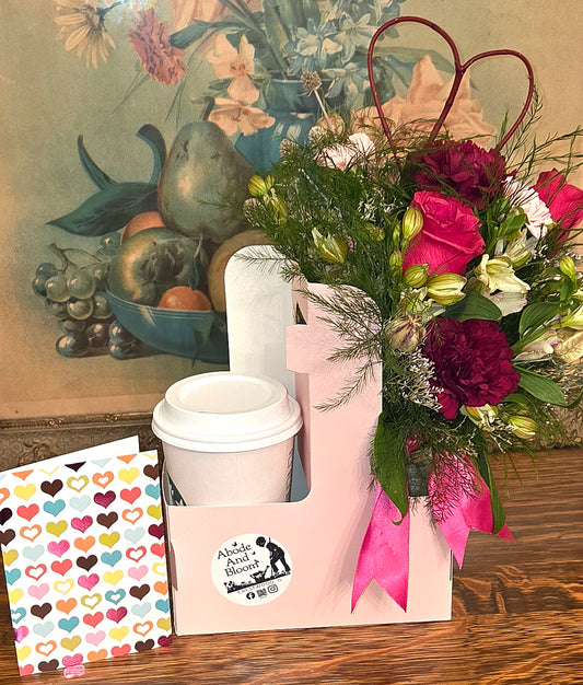 Floral arrangement with a pink carrier, coffee to go, and colorful heart card.