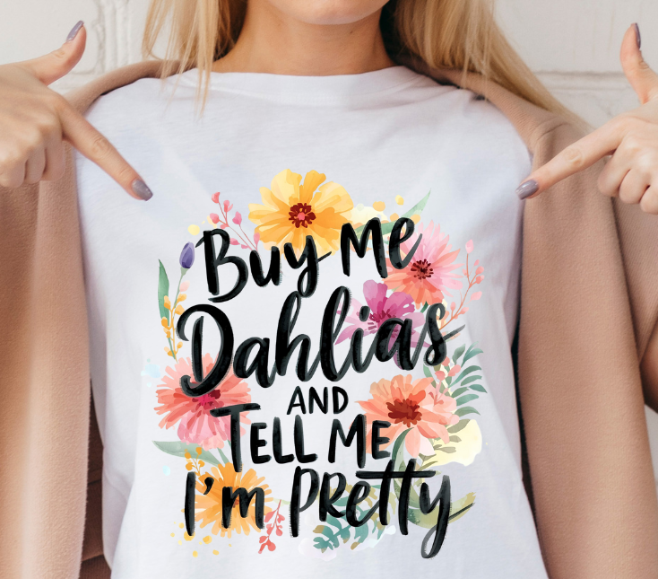 Woman wearing a white t-shirt with floral text design, pointing at herself.