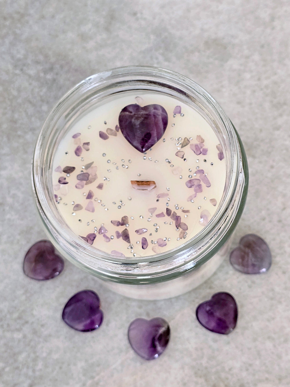 Candle in a glass jar with purple heart-shaped stones decorations on a gray surface